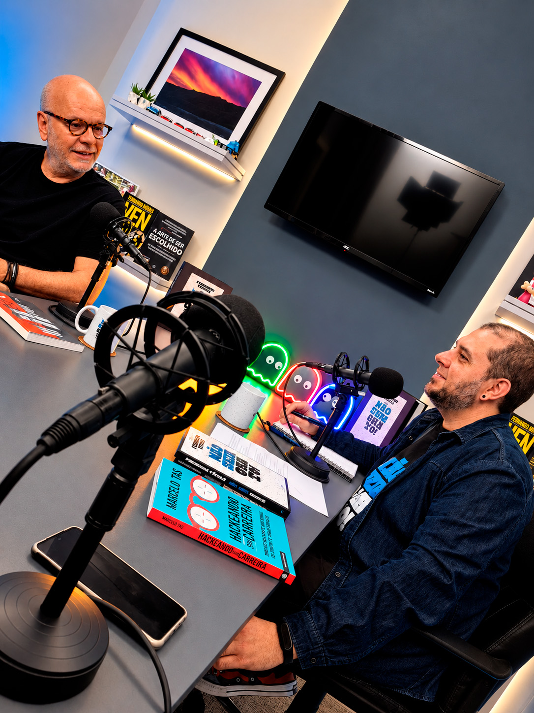 Duas pessoas conversam ao microfone durante a gravação de um podcast