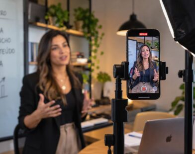Celular em tripé grava apresentação vertical de profissional em ambiente de escritório, com iluminação e roteiro ao fundo.