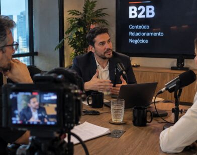 Três profissionais participam de uma gravação de podcast sobre negócios em uma sala de reuniões, com câmeras e microfones.
